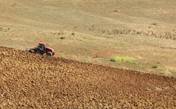Agricultural worker driving red tractor, turning fertile ground during sunny day, cultivating farmland with precise mechanical movements for upcoming crop planting season - Powered by Adobe