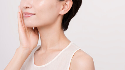 片手で頬を触っているアジア人女性。スキンケア。