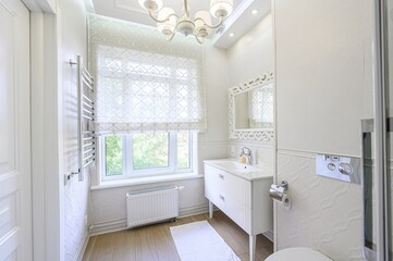 Bright, white bathroom with classic details. Features a vanity, ornate mirror, toilet, and a glass-enclosed shower. Natural light through a window adds to the airy feel.