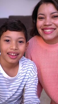 Point of view of young mother and son on a video call with their family, connected in the distance. Latin American single mom and child looking at camera waving happily. Vertical video.