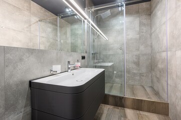 Modern bathroom featuring gray tiles, a sleek vanity with a white sink, and a glass-enclosed...