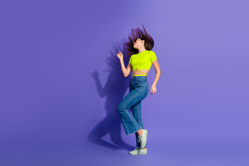 Young woman dancing energetically against a vivid purple background, in a fashionable casual outfit