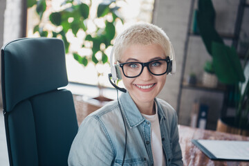 Smiling young woman with a headset in a modern workspace, demonstrating professionalism and...