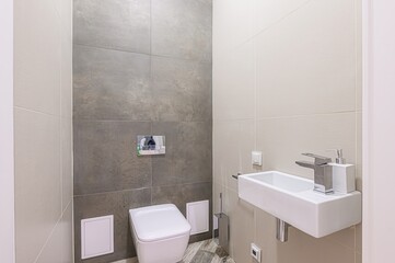 Modern bathroom featuring gray and beige tiles, a wall-mounted toilet, and a minimalist sink.