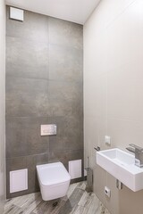 Modern bathroom featuring gray and beige tiles, a wall-mounted toilet, and a minimalist sink.