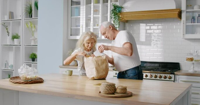 Organic food for stay healthy in old age, happy aged wife and husband in kitchen . Modern interior of apartment, elderly people preparing to cooking dinner, unpacking purchase from grocery store