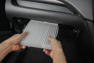 Close-up of man's hand changing or checking the air conditioning filter in car cabin. Car check and maintenance.