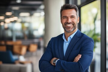Fototapeta premium A confident businessman man smiles with his arms crossed, dressed in a blue suit jacket, light blue collared shirt, and wristwatch.