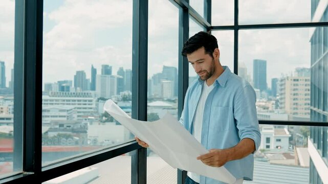 Professional engineer smiling while looking at skyscraper view. Skilled architect in casual outfit looking, planning plan project while standing near panorama window with city scape. Tracery