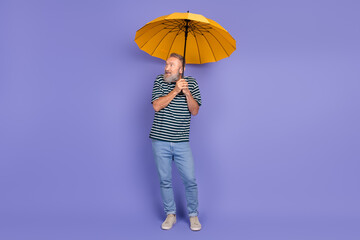 Elderly man holding a yellow umbrella, wearing a striped shirt and jeans, standing on a vibrant...