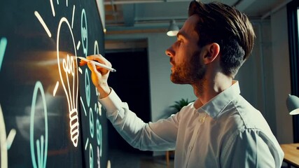 Focused businessman drawing a light bulb and other icons on an interactive whiteboard, symbolizing innovation and idea generation in a modern office environment