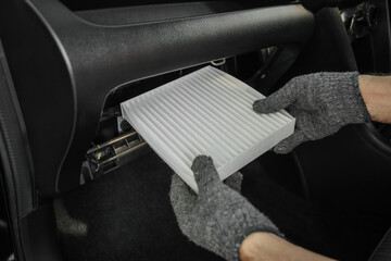 Hands are removing and replacing the air conditioning filter in a car. Checking and maintaining the car air conditioning.