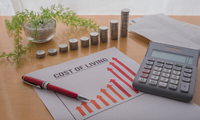 A paper showing a graph of the rising of the rising  cost of living. Coins , calculator , pen on the table