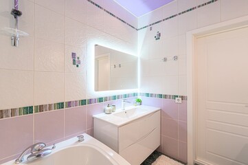 bright bathroom with a modern bathtub, white tiles with purple accents, and a backlit mirror. The ceiling is painted a soft lilac.