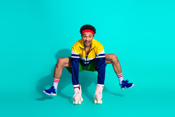 Cheerful young man roller skating in retro outfit with vintage style on vibrant teal background showcasing athletic