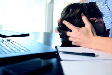 man at computer holding his head, work online. a man is working on a laptop, there is a notebook...