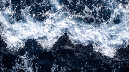 Aerial view shows ocean waves crashing against dark rocks creating white foam.