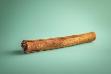 A single cinnamon stick rests on a smooth turquoise surface