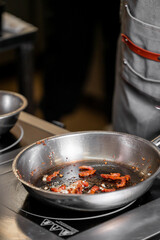 A close-up of a stainless steel frying pan with sautéed sun-dried tomatoes, showcasing cooking preparations in a professional kitchen environment.