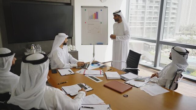 Cinematic video of a group of businessmen from UAE during an corporate meeting in an office. Locals men in kandura making business together.