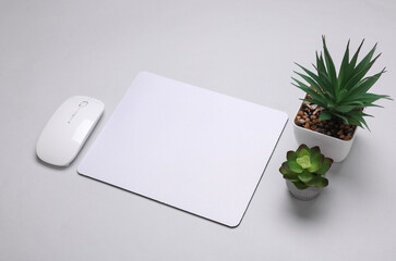 Mockup of white blank computer mouse pad or mat with props, decorative plants on gray background.