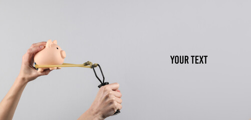Hands holding slingshot with piggy bank on gray background. Business concept. Copy space for your...
