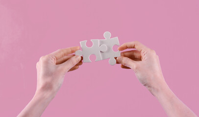 Woman's hands hold puzzle pieces on a pink background. Business concept, teamwork