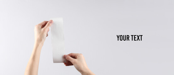 Women's hands hold a white empty shopping receipt mockup on a gray background. Copy space for your...