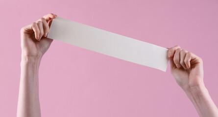 Women's hands hold white empty shopping receipt mockup on pink background. Template for design. Places for text