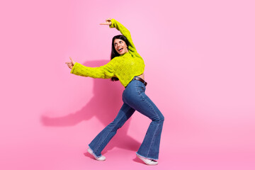 Happy young woman in stylish yellow knit sweater and jeans posing playfully against pink...
