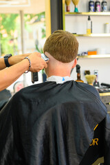 A barber giving a man a haircut with an electric razor, shaping the hair at the nape of his neck in a barbershop setting.