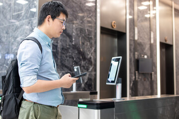 An Asian business man passes through the access control turnstile of the office building by facial...