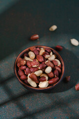 Raw peanuts in wooden bowl on dark green textured background