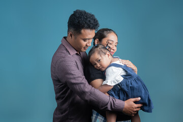 Happy Indonesian parents hugging their daughter with love and care in a studio setting. Warm, emotional moment showing family bond, parenting, and affection.
