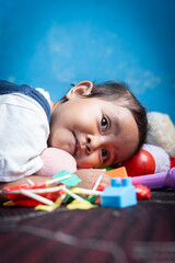 Obraz premium An Asian toddler girl lies on her stomach, appearing tired after playtime. A soft and quiet moment reflecting the calm and natural side of childhood.