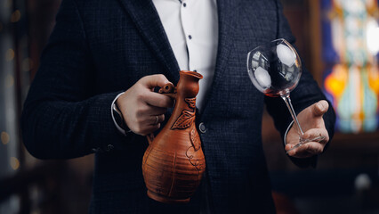 Male sommelier pouring red wine from georgian clay jug into glass in elegant setting