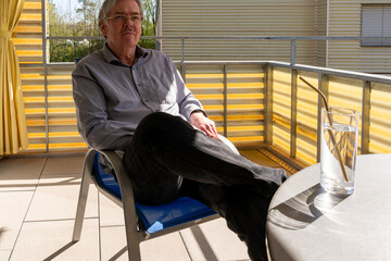 Male on balcony, with tousled hair, thoughtful facial expression, on a sunshiny day..