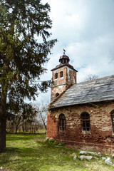 Naklejka premium Old brick church with a bell tower surrounded by trees on a cloudy day. Ukraine.