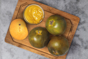 Top view Fresh lucuma fruits and a bowl of lucuma pulp on a wooden cutting board, placed on a stone...