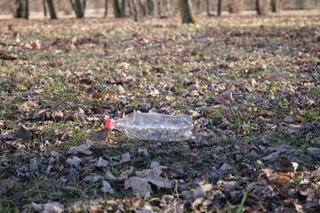 Obraz premium An empty plastic bottle on the ground in a city park. Environmental pollution. Environmental problem. City buildings side by side