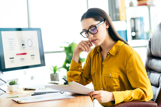 Professional young businesswoman analyzing data at her desk in modern office environment emphasizing strategic focus and creativity