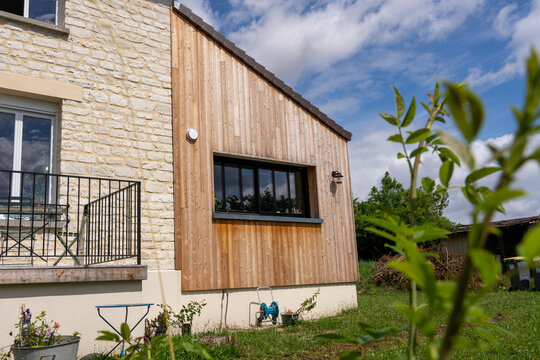 Extension moderne d&rsquo;une maison avec bardage en bois, contrastant harmonieusement avec la structure ancienne en pierre.