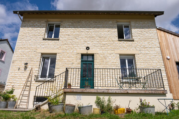 Façade d’une maison en pierre beige clair avec escalier menant à la porte d’entrée, décorée de plantes en pot dans un esprit campagnard chaleureux.