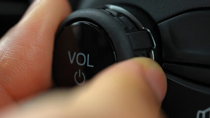 Macro close-up of woman's fingers turning the volume of the car radio. Turning down or up the vehicle audio system volume.