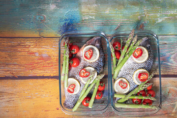 Green asparagus on fresh large dorado fish, tilapia, carp in baking dish with cherry tomatoes,step by step recipe instructions, top view on an old wooden table