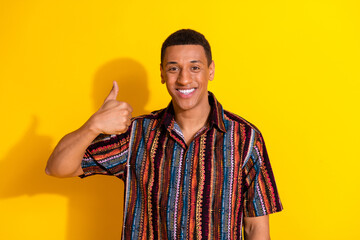 Smiling young man in a colorful casual shirt giving a thumbs up gesture against a vibrant yellow...