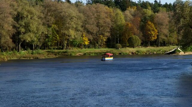 A Small Colorful Tourist Boat - Raft, is Sailing Along the River in Autumn. Valmiera is One of the Oldest Cities in Latvia, Having Been a Member of the Hanseatic League.