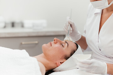 Naklejka premium Cosmetology beauty procedures. Lady receiving rejuvenation anti aging treatment, facial chemical peel therapy in beauty salon or medical center. Wellness. Mask with retinol. Free copy space