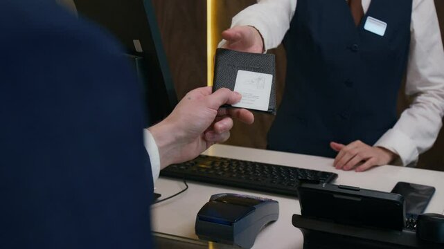 Close up over the shoulder view of guest receiving key card and passport from receptionist after check-in process at hotel front desk