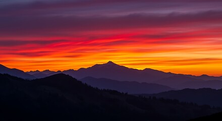 Mountains under fiery sunset.  Multiple mountain ranges silhouetted against vibrant, colorful, and stunning twilight sky. 